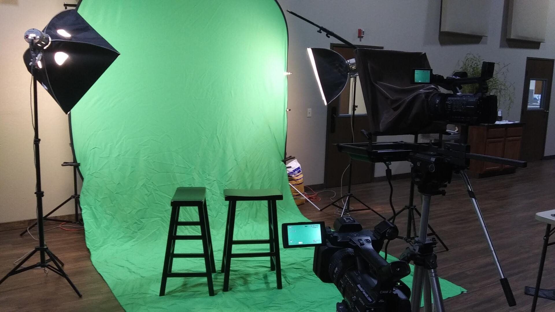 A green screen is behind two stools in a studio.