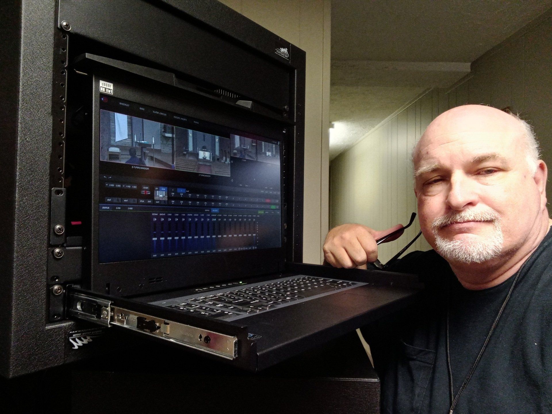 A bald man with a beard is standing next to a laptop