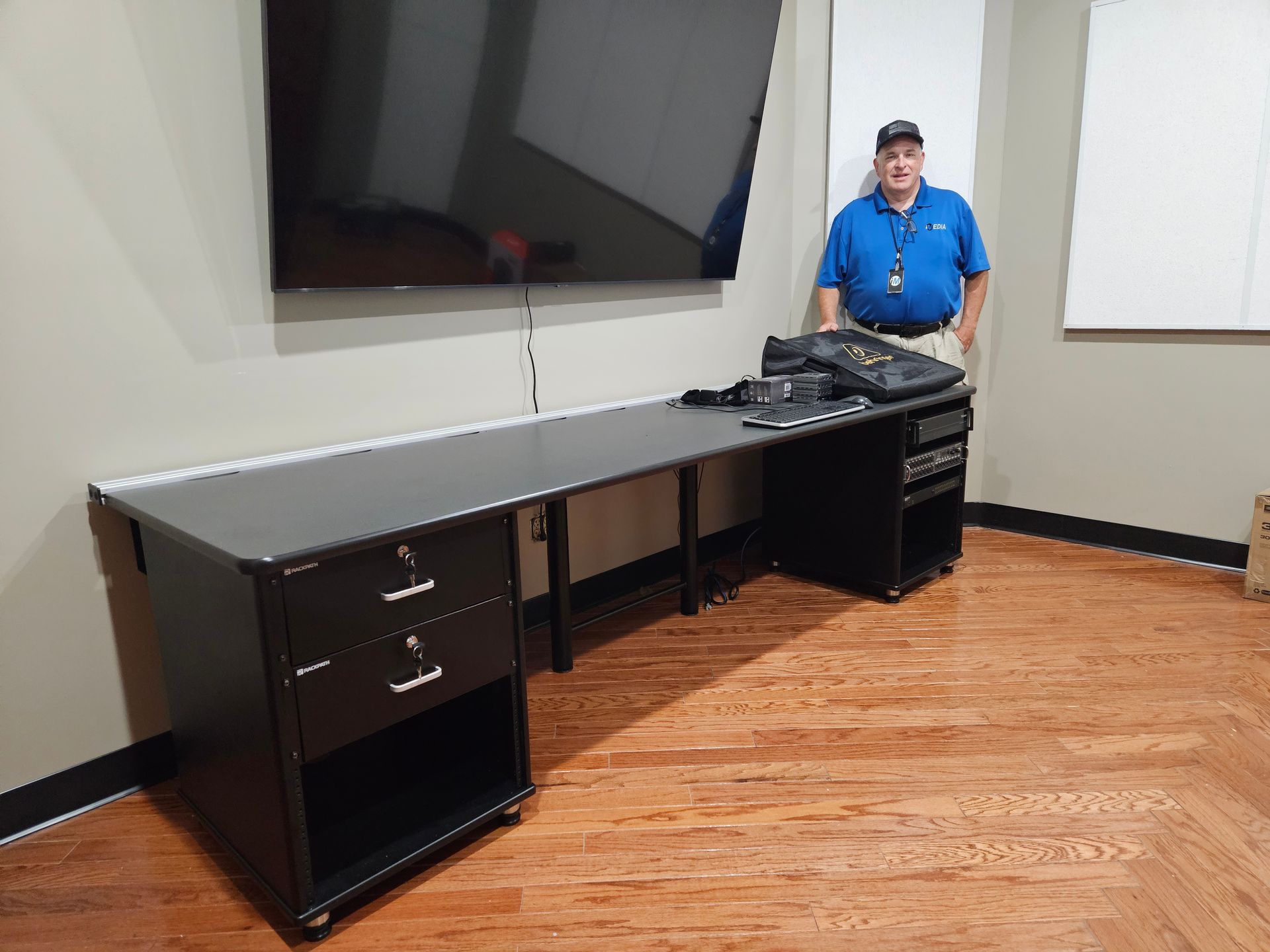 A man is standing next to a 9ft custom made desk in new TV control room.