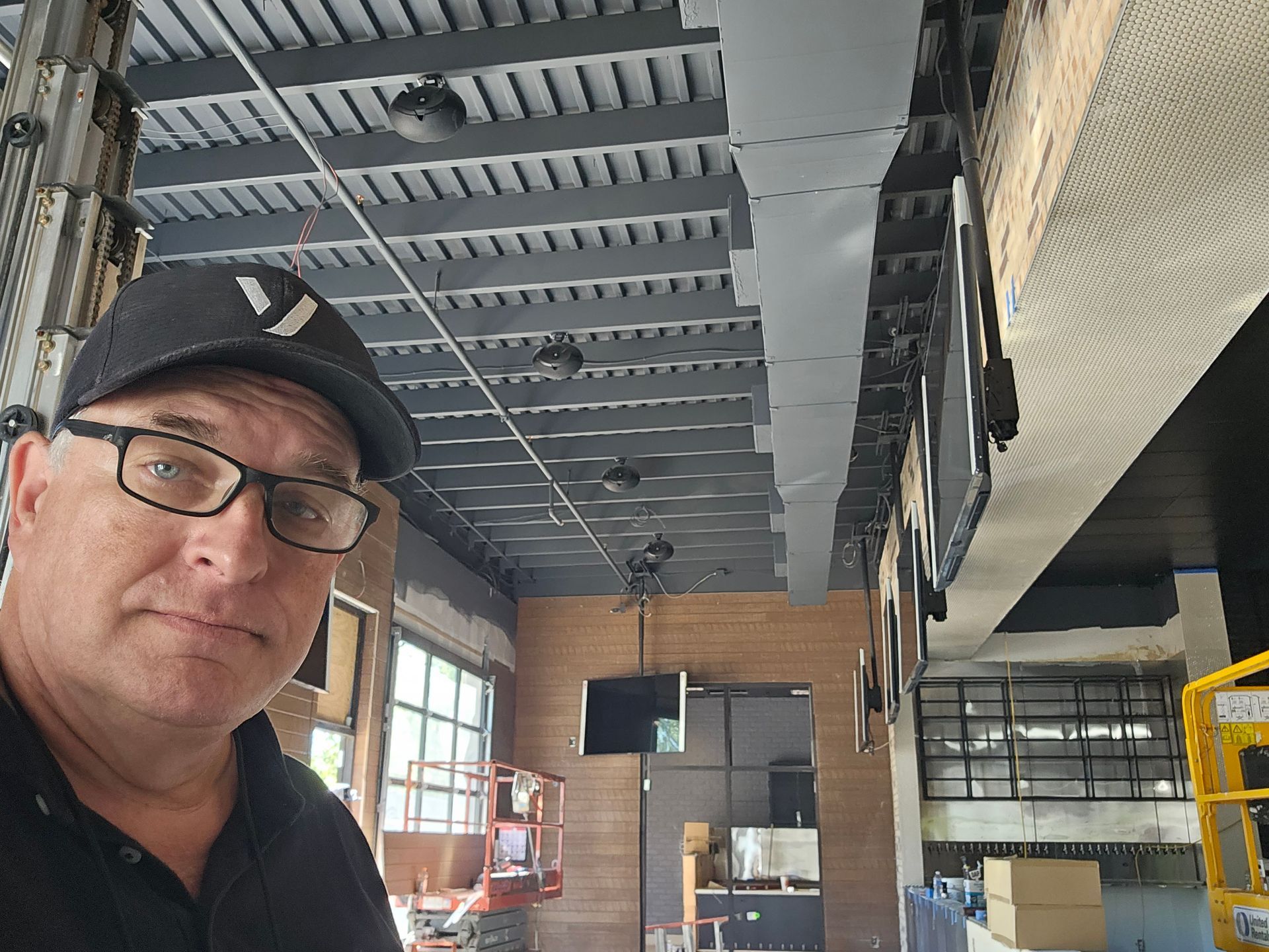 A man wearing glasses and a hat is taking a selfie in a building under construction.
