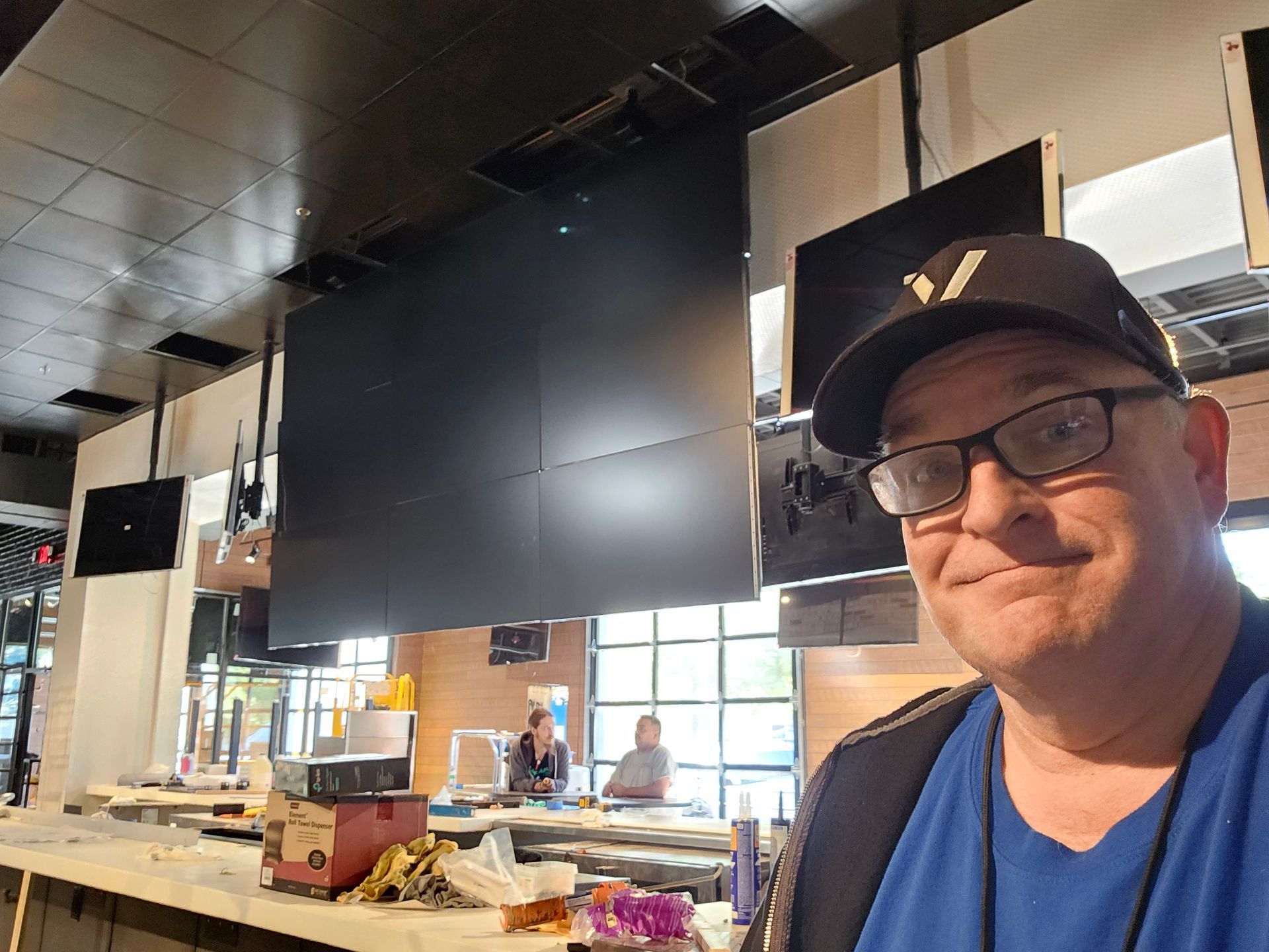 A man wearing glasses and a hat is taking a selfie in a restaurant.