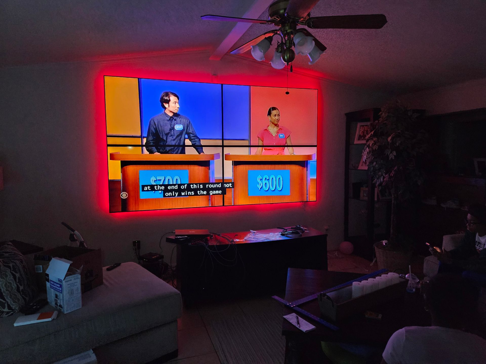 A living room with a projector screen showing a game show called jeopardy