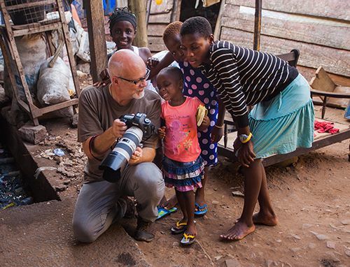 A man is kneeling down to take a picture of a group of children.