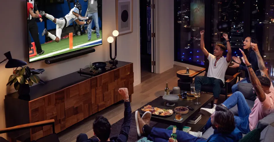 A group of people are sitting on a couch watching a baseball game on a television.