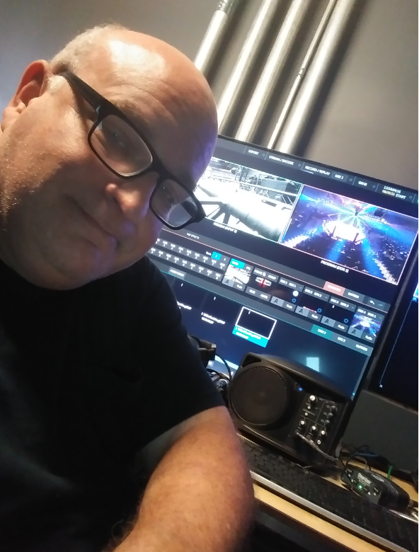 A bald man wearing glasses is sitting in front of a computer screen
