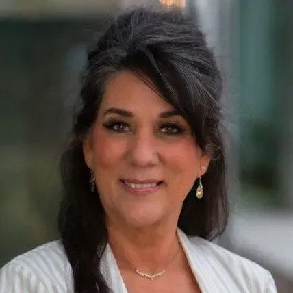 A woman wearing a white jacket and earrings is smiling for the camera.