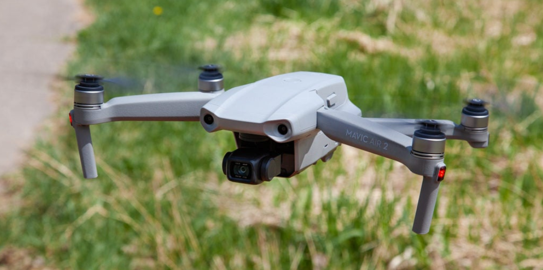 A small drone is flying over a field of grass.