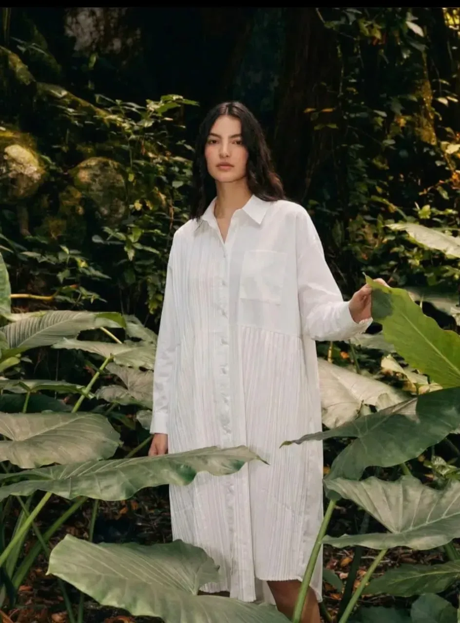 Femme en robe blanche se tenant parmi une végétation tropicale luxuriante dans un jardin forestier