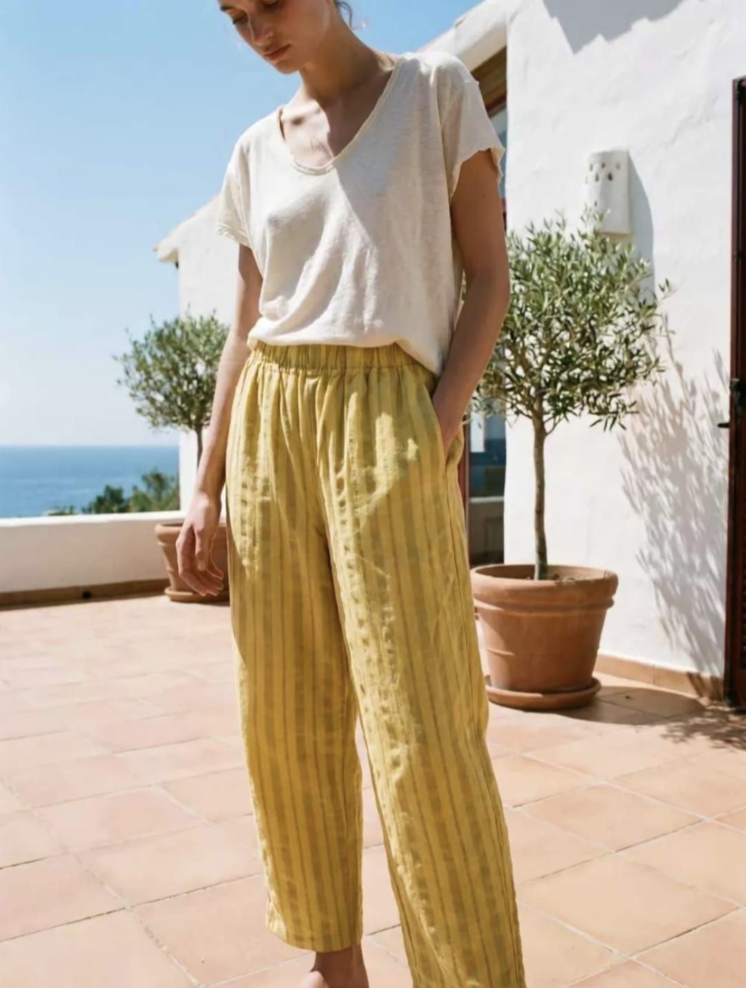 Personne appuyée contre un mur, vêtue d'un haut blanc et d'un pantalon à motifs jaunes, au soleil