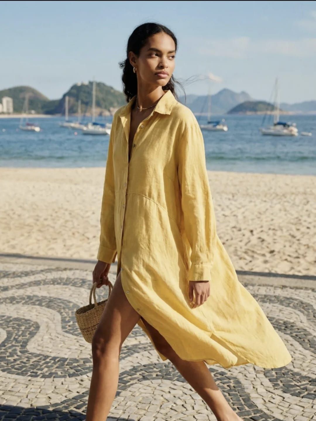 Une femme en robe verte marche sur une véranda en bois aux balustrades blanches et à la végétation tropicale.
