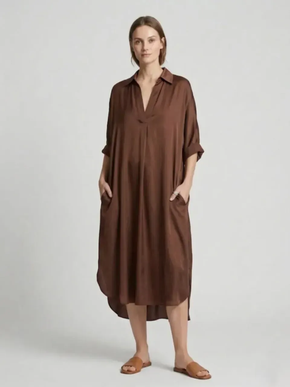 Femme en robe-chemise midi marron et sandales beiges se détachant sur un fond gris clair