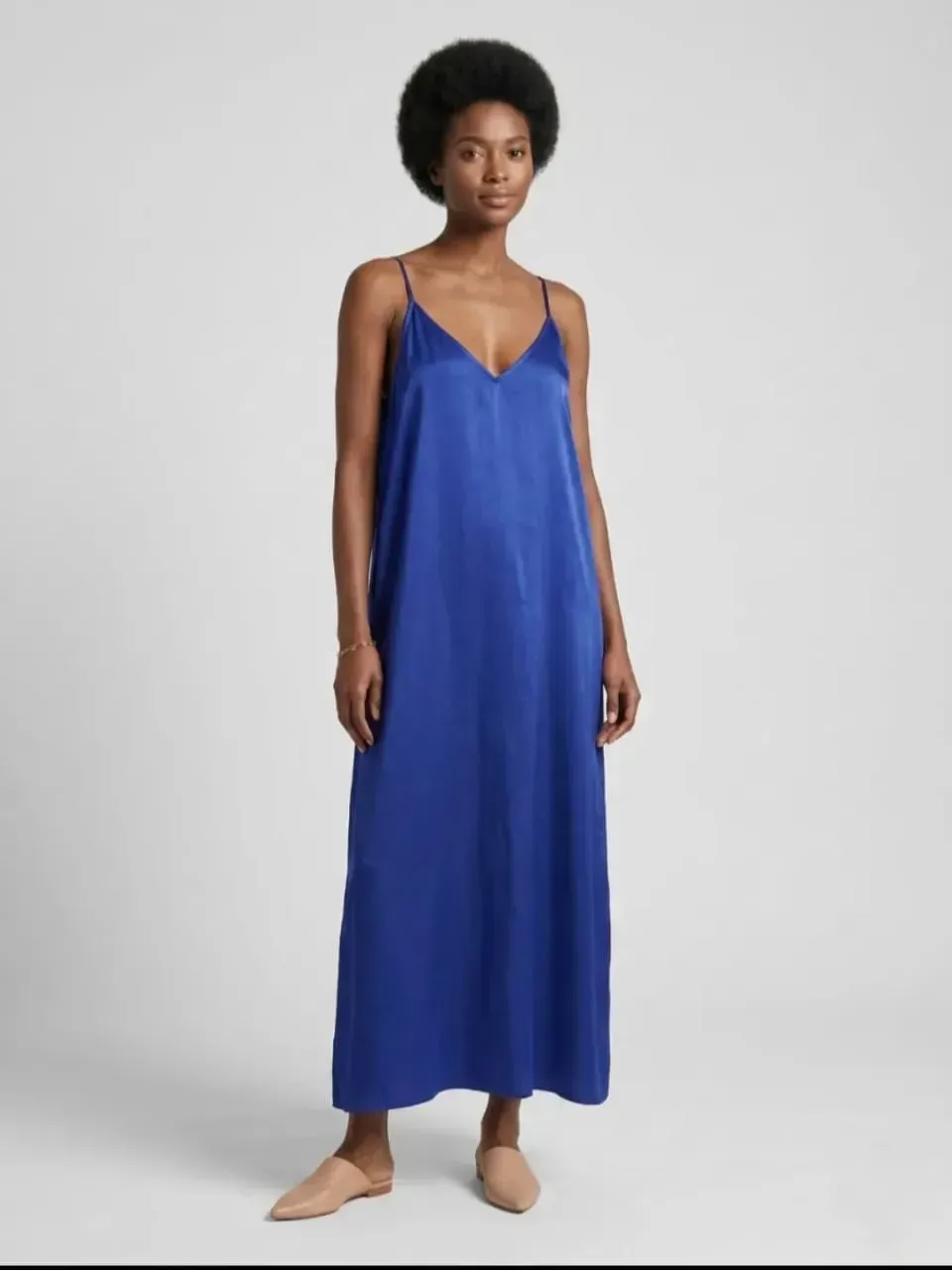 Femme en robe longue bleue sans manches, pieds nus sur fond gris