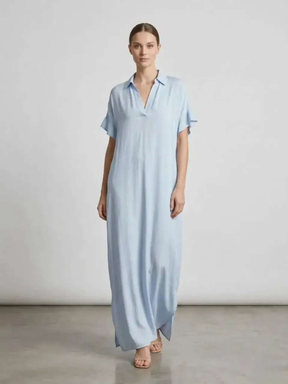 Femme en robe ample bleu clair se tenant devant un fond gris uni de studio