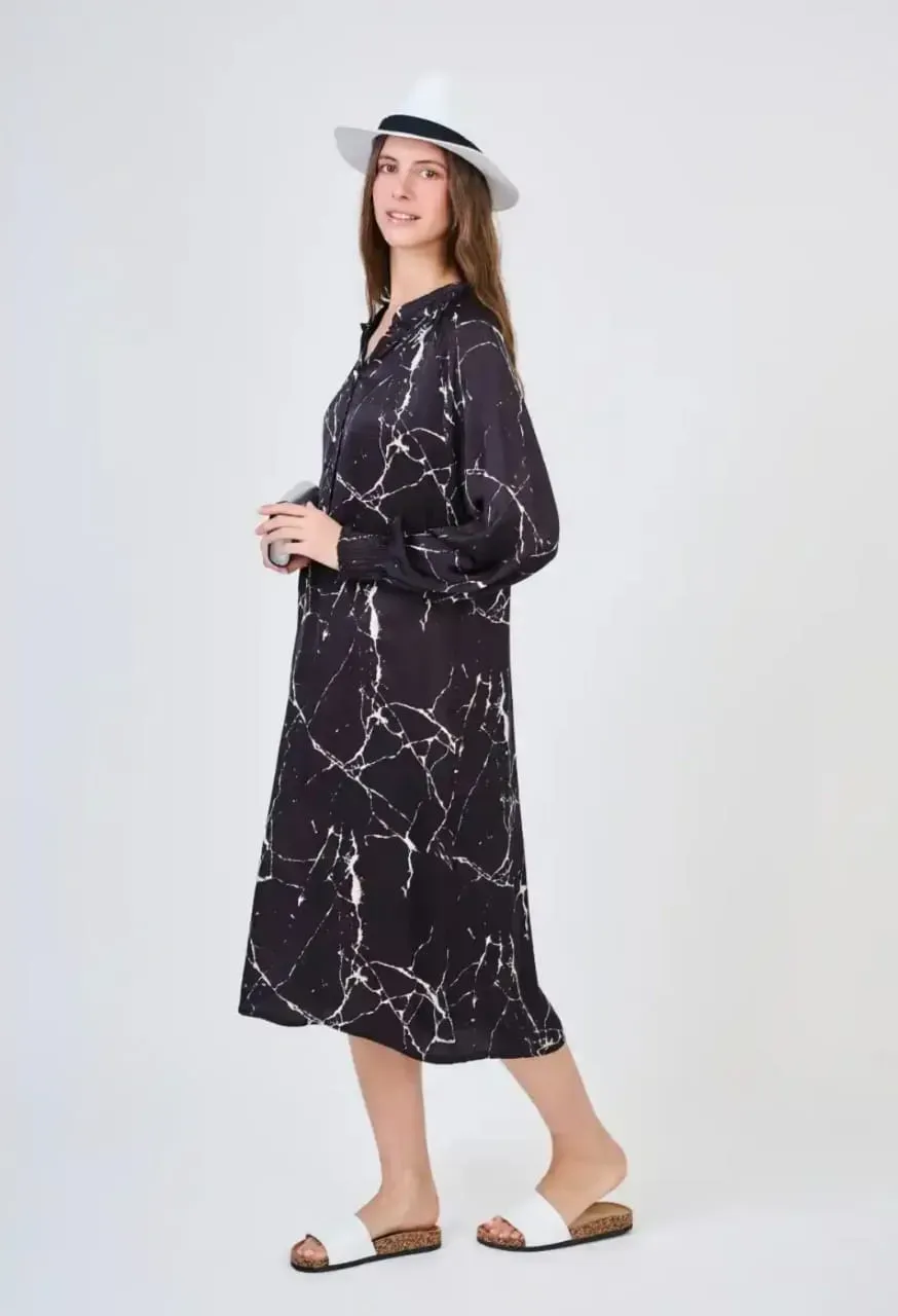 Femme en robe noire à motifs et chapeau blanc marchant en sandales blanches sur fond clair
