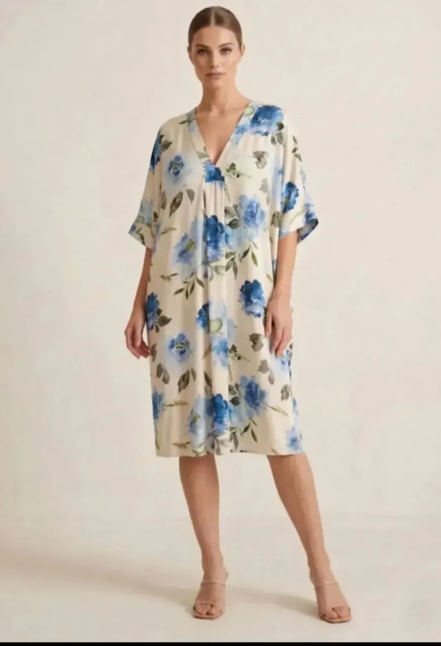 Mannequin portant une robe portefeuille crème à fleurs bleues et des sandales sur fond uni