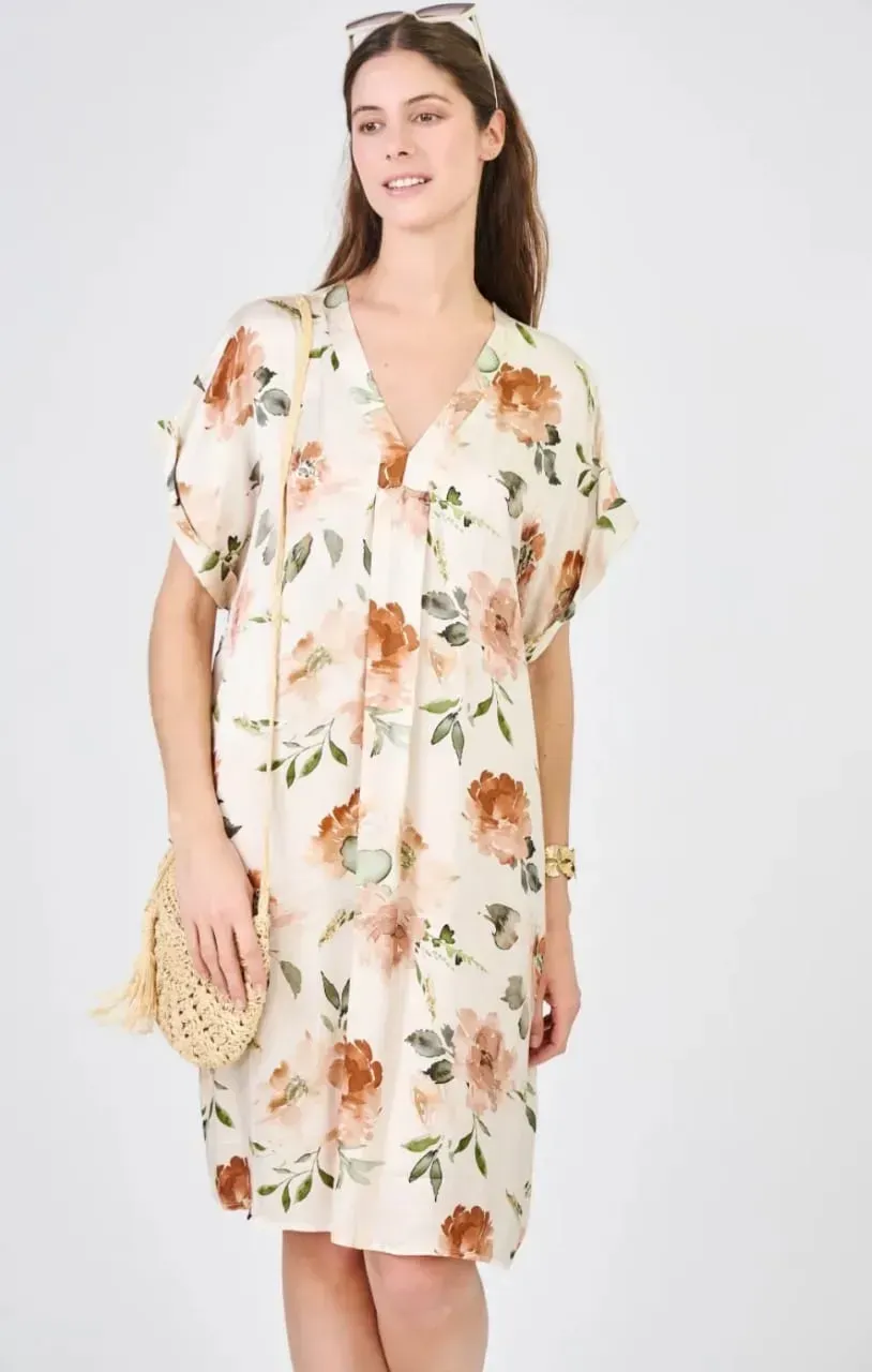 Femme vêtue d'une robe blanche à fleurs tenant un sac en osier sur fond clair.