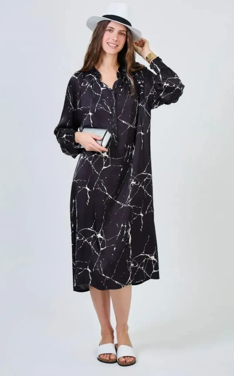 Femme portant une robe midi noire à motifs et un chapeau blanc, tenant une pochette sur fond blanc