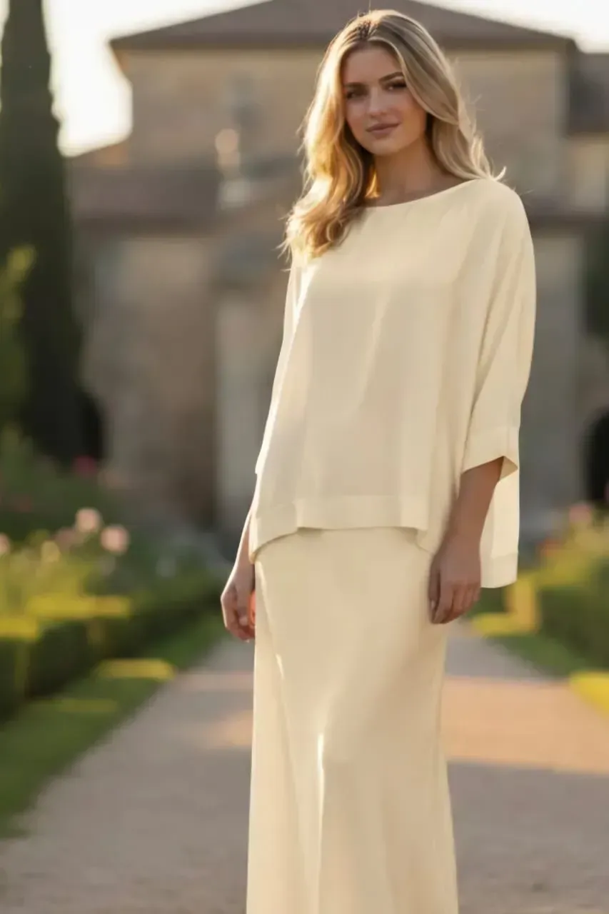 Femme vêtue d'une tenue crème, debout à l'extérieur sur un chemin ensoleillé.