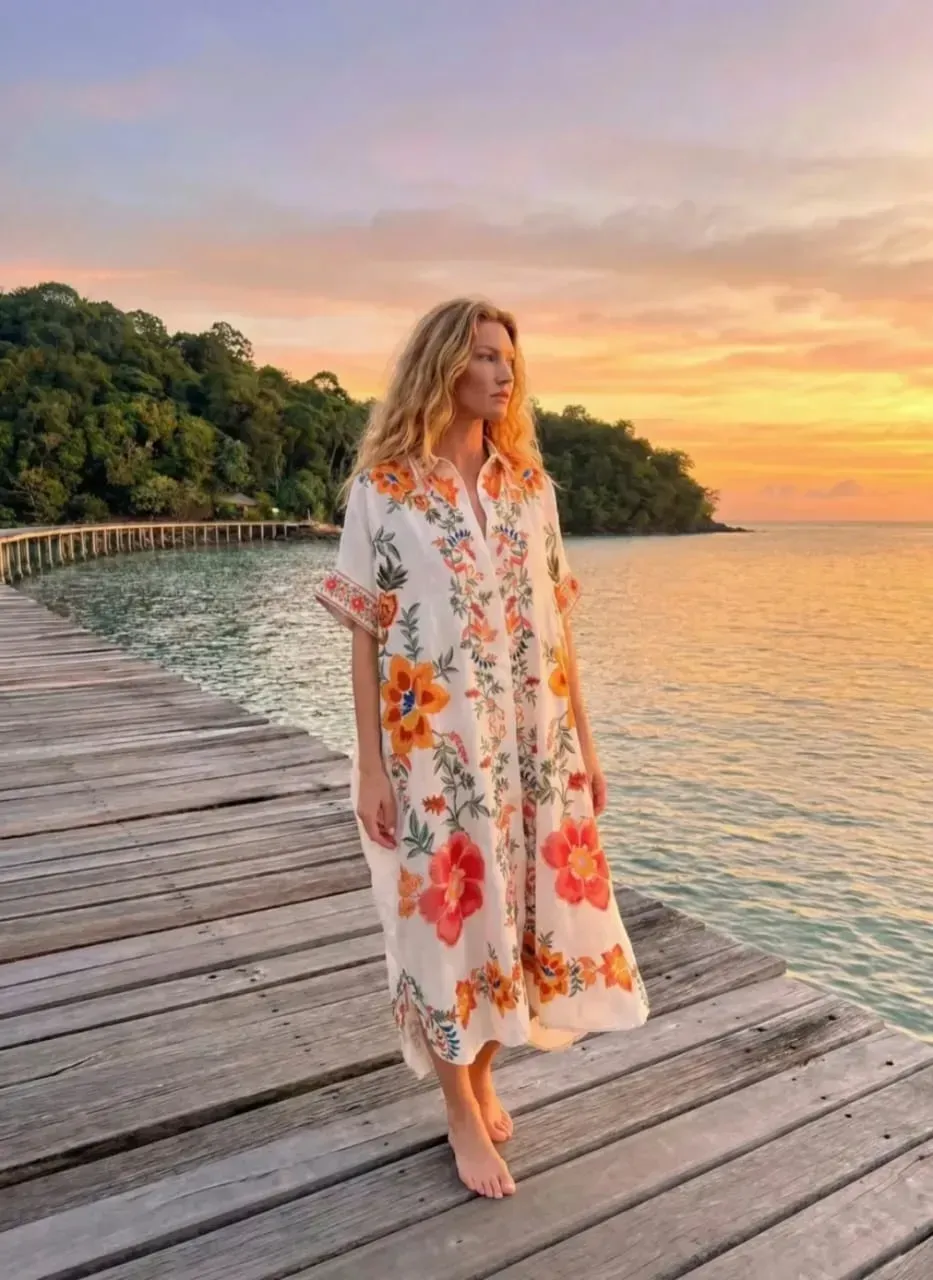 Femme en robe à fleurs debout sur une jetée en bois au coucher du soleil, au bord d'une eau calme.