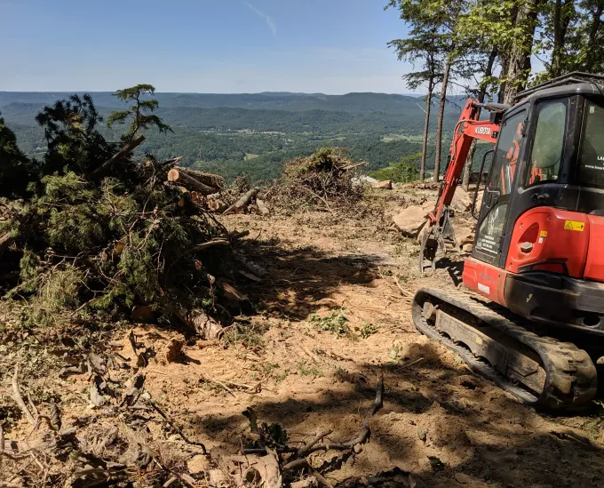 A red and black excavator is sitting on top of a dirt hill.