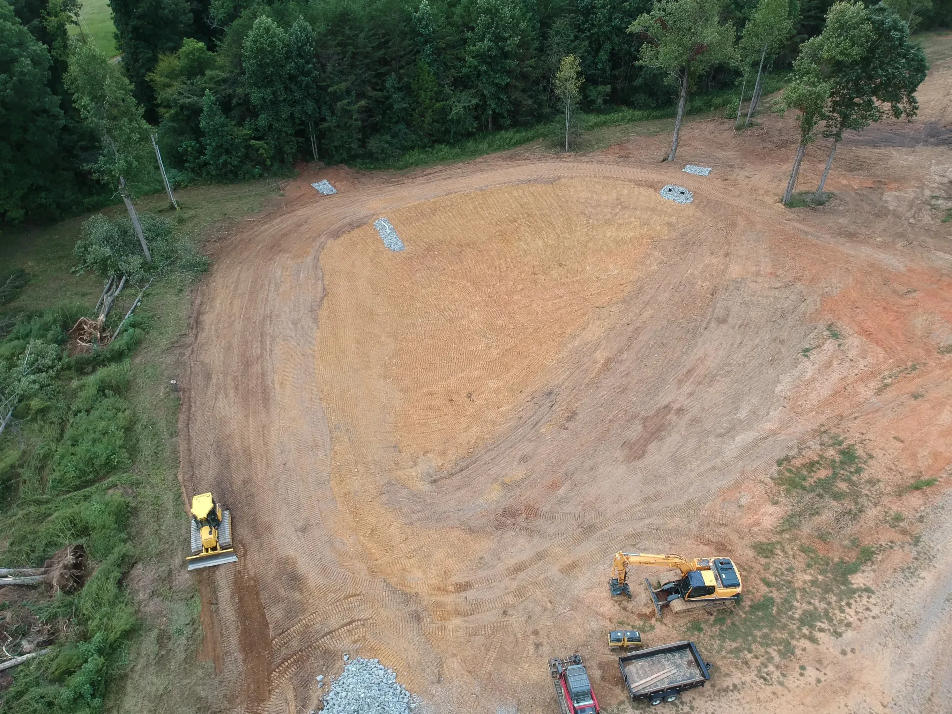 An aerial view of a construction site with a lot of dirt and trees in the background.