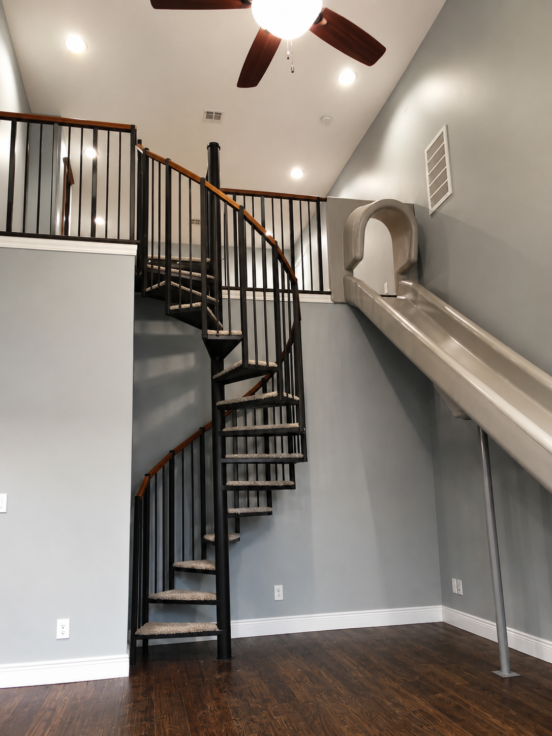 Interior loft with a spiral staircase, slide, gray walls, wood floors, and ceiling fan
