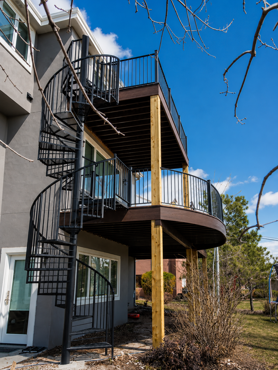 Spiral staircase beside a curved wooden balcony on a modern apartment building under a blue sky.