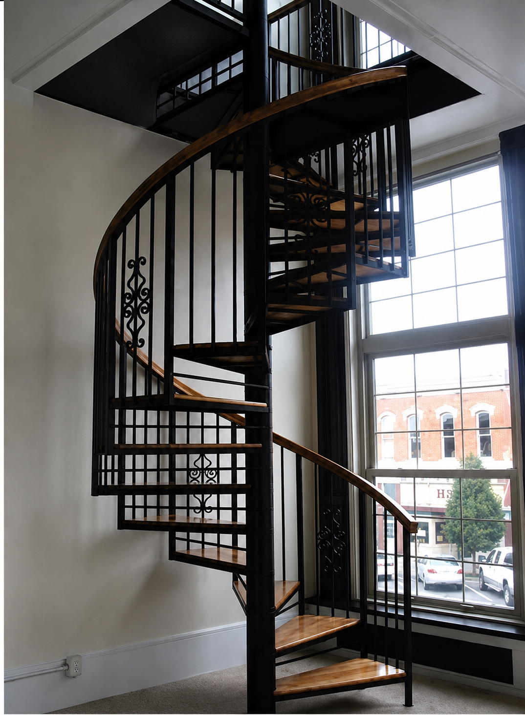 Curved black spiral staircase beside tall windows in a bright interior room