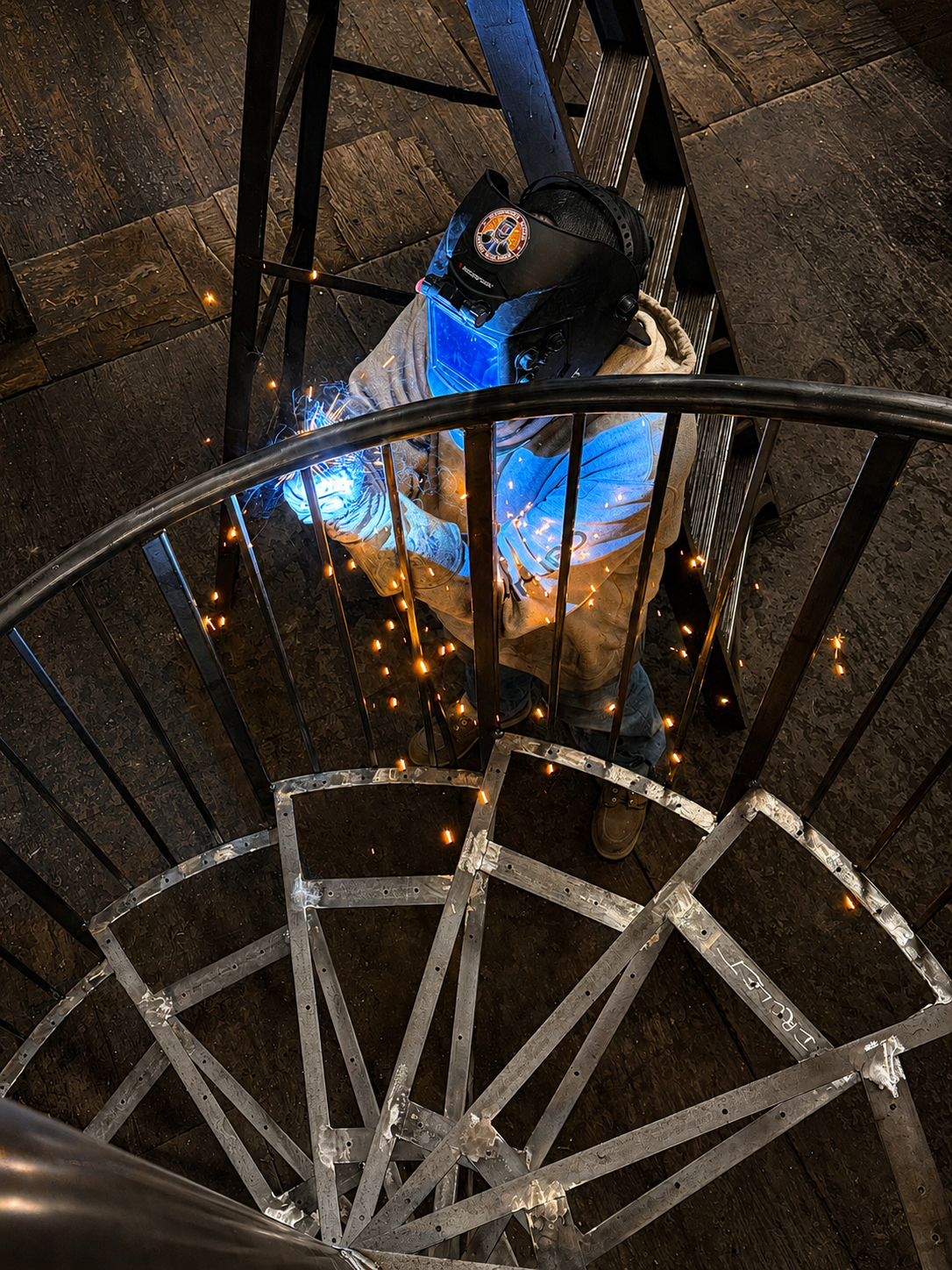 Person in blue jacket climbing a spiral metal staircase at night, viewed from above