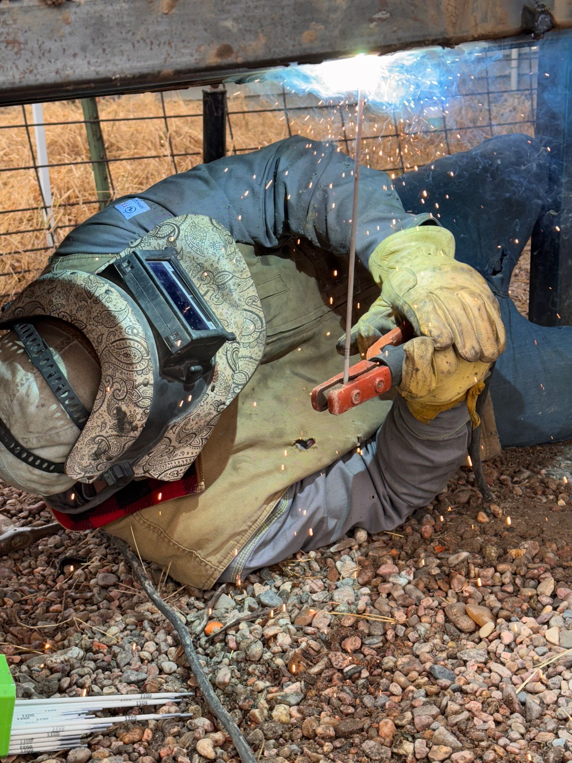 Welder in blue protective gear welding metal beams, sparks flying in an industrial workshop