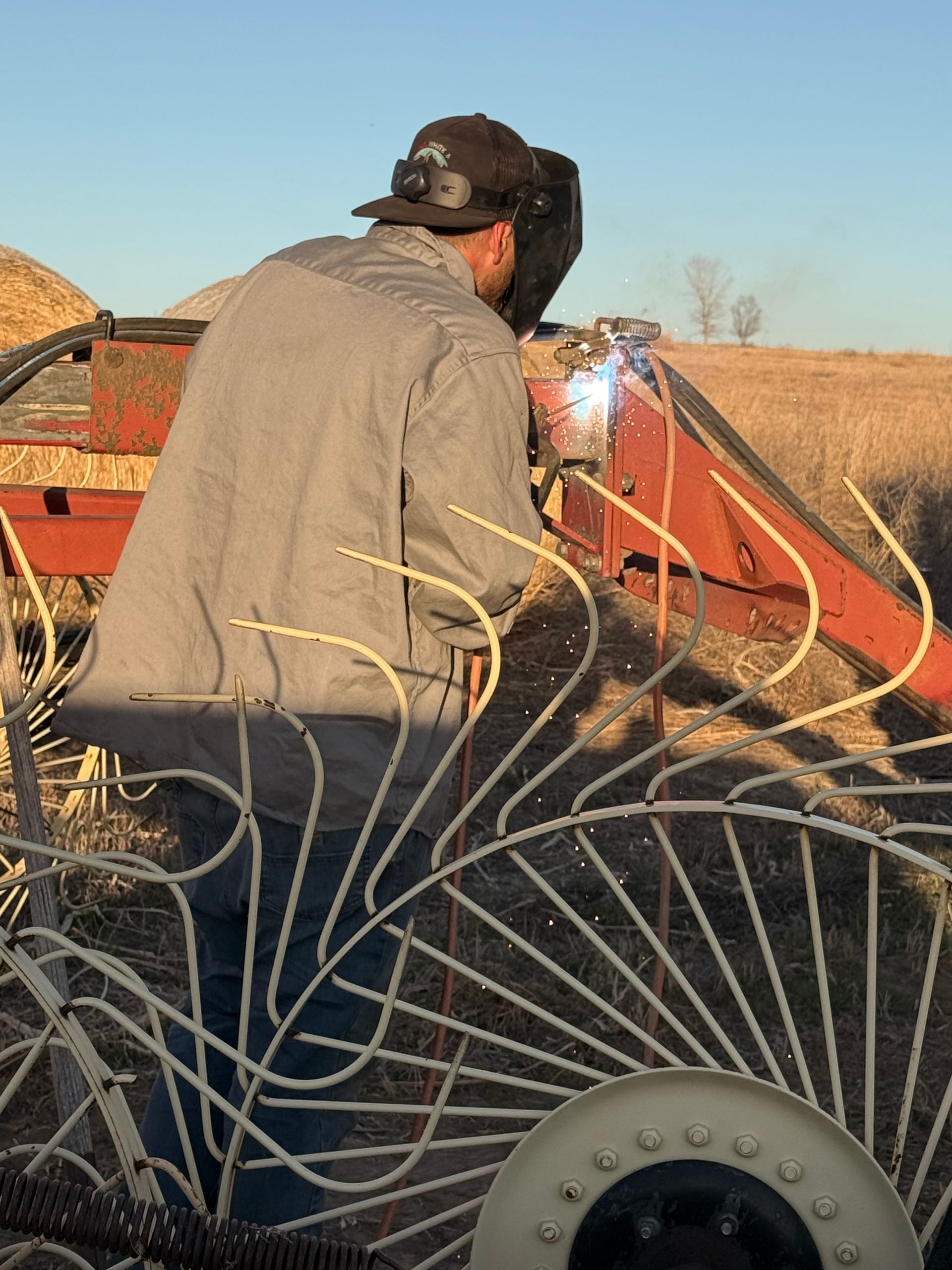 Person welding on farm equipment in a dry field at sunset