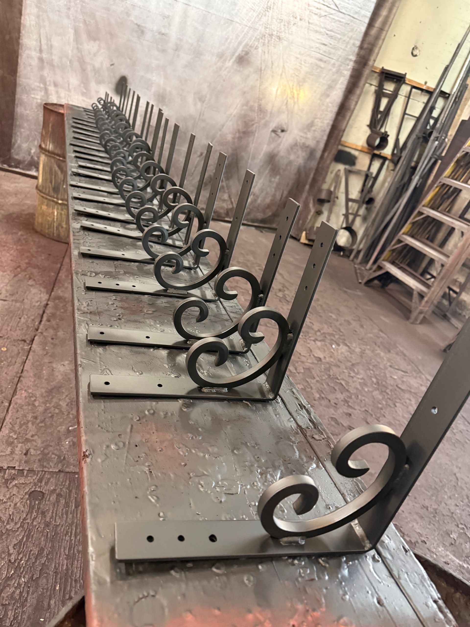 Row of black metal scrollwork fence panels lined up in a workshop on a concrete floor