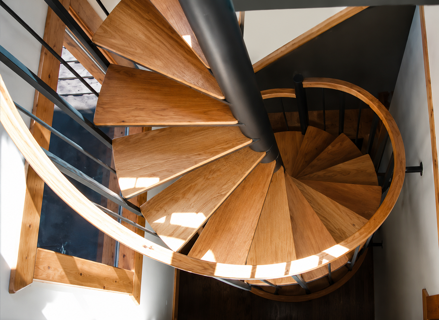 Top-down view of a wooden spiral staircase with black metal railing and white walls