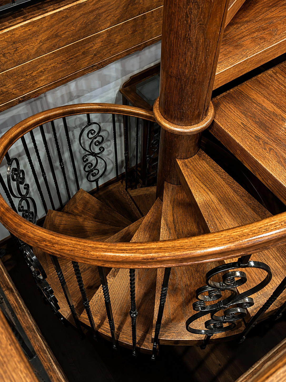 Spiral wooden staircase with black wrought-iron railings and polished wood finish