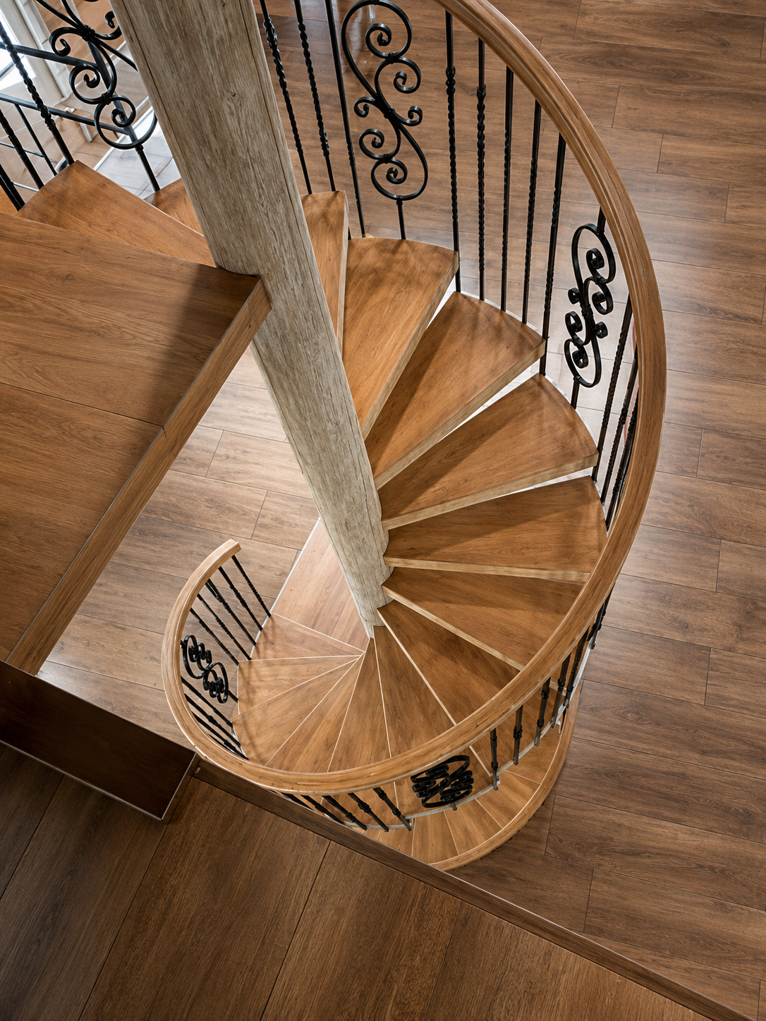 Spiral wooden staircase with ornate black railings viewed from above.
