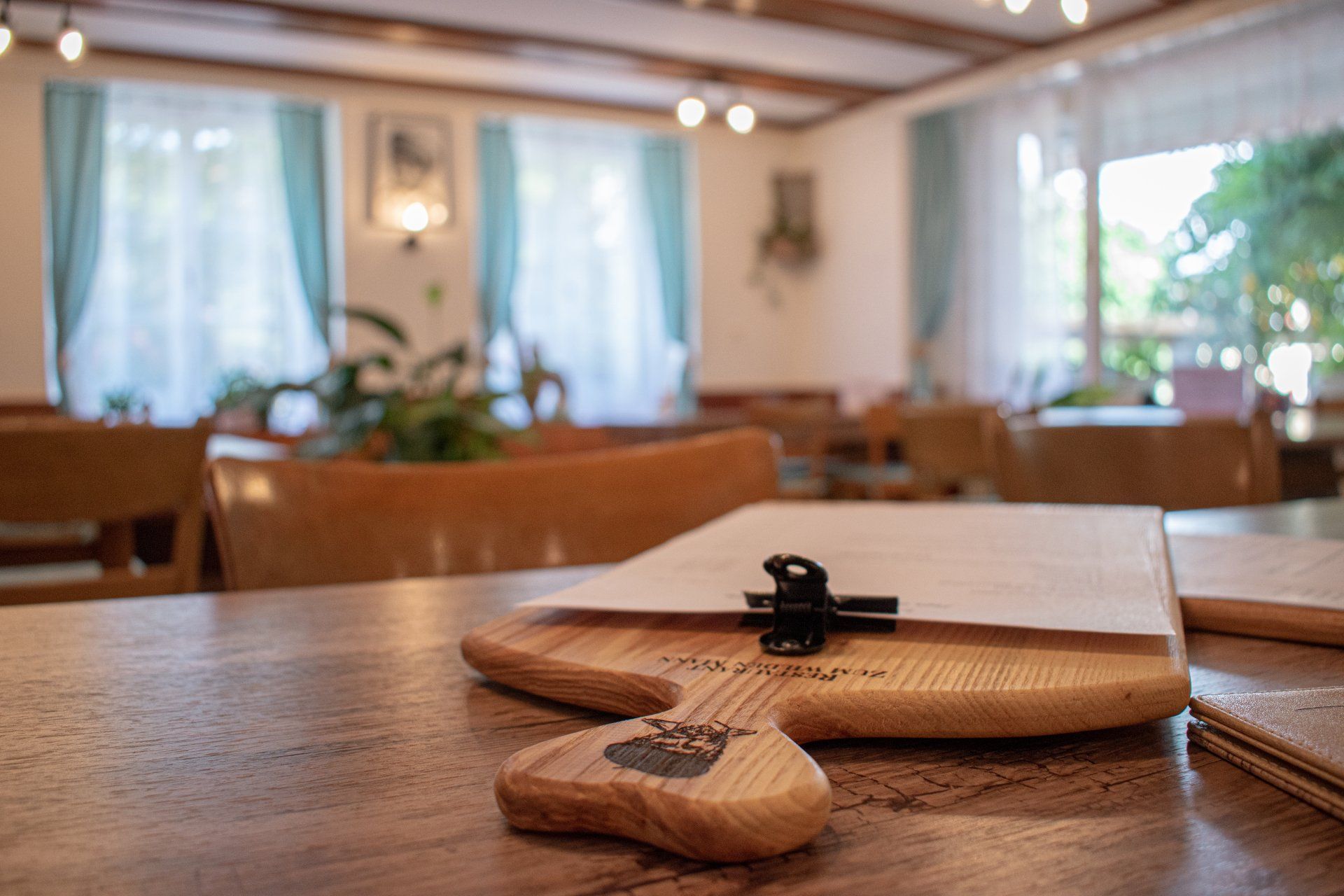 Holztisch mit einem kleinen geflochtenen Platzset, einer Serviette und einer schwarzen Klammer in einem hellen Café