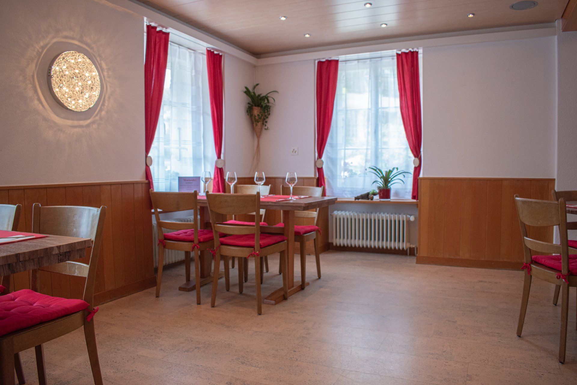 Leerer Cafébereich mit roten Vorhängen, Holzstühlen und Tischen an den Fenstern