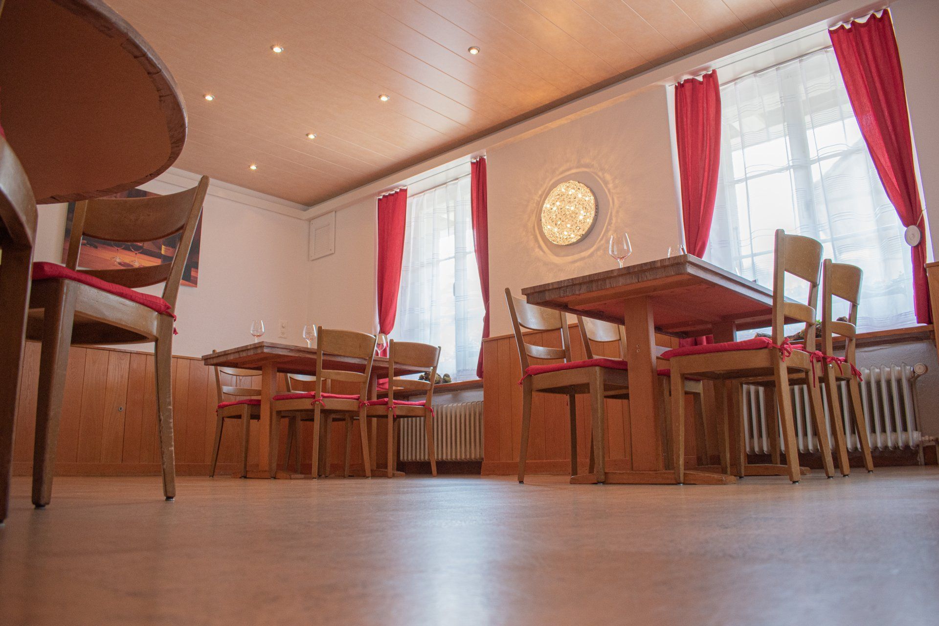 Leerer Speisesaal mit Holztischen, Stühlen, roten Vorhängen und einer schrägen Ansicht des Bodens von unten