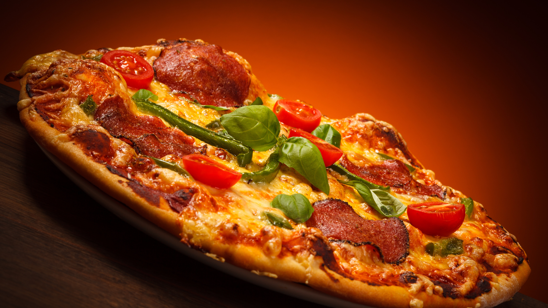 A pizza with pepperoni , tomatoes , basil and cheese on a plate.