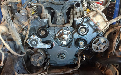 Front view of an automotive engine block with the serpentine belt removed, showing pulleys, the water pump, and oil filter.
