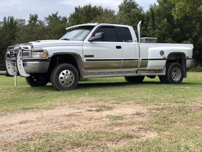 A white, dual-rear-wheel Dodge Ram pickup truck with a brush guard and exhaust stack parked on grass.