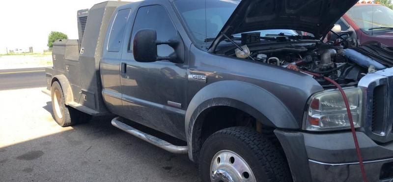 A grey Ford Super Duty truck with an open hood, parked outdoors on a paved lot.