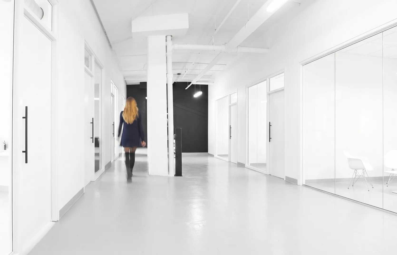 Couloir blanc lumineux où une personne seule s'éloigne vers une porte sombre