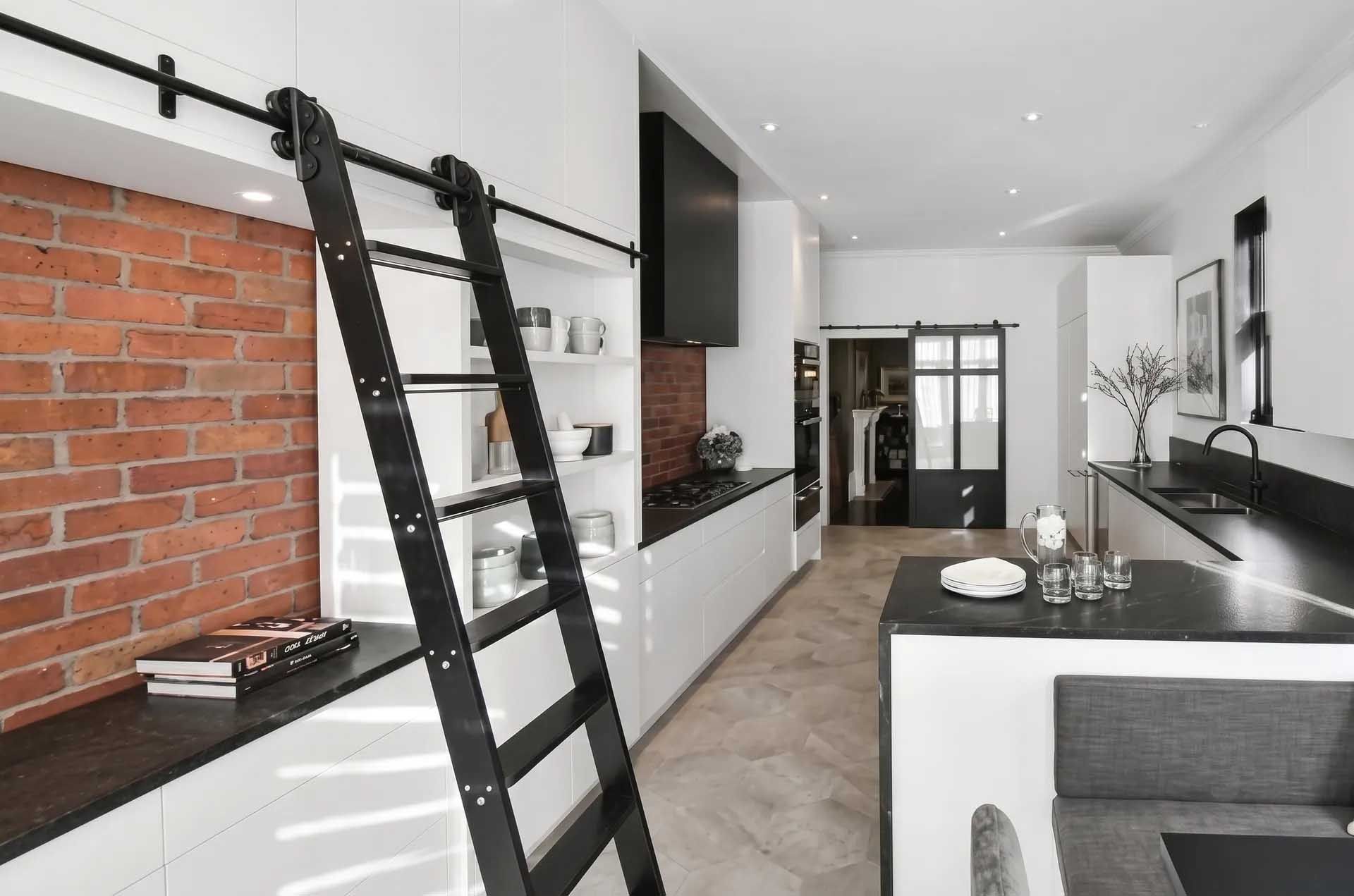 Cuisine et salle à manger modernes de style loft avec échelle noire, mur de briques et armoires blanches.