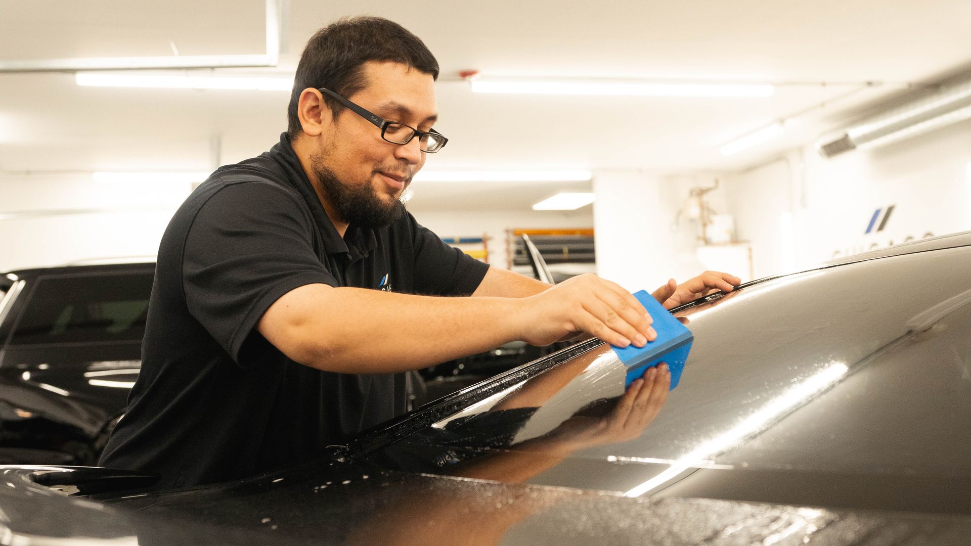 A man is cleaning the windshield of a car with a blue cloth.