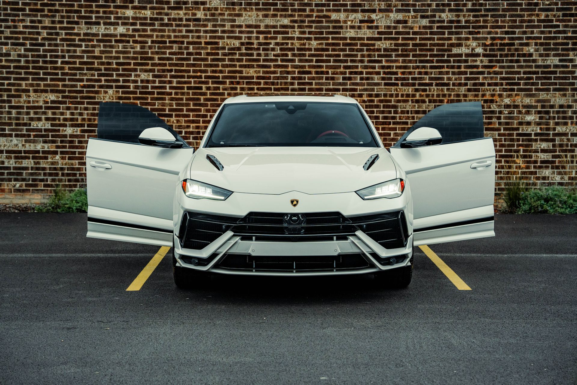 A white lamborghini urus is parked in a parking lot with its doors open.