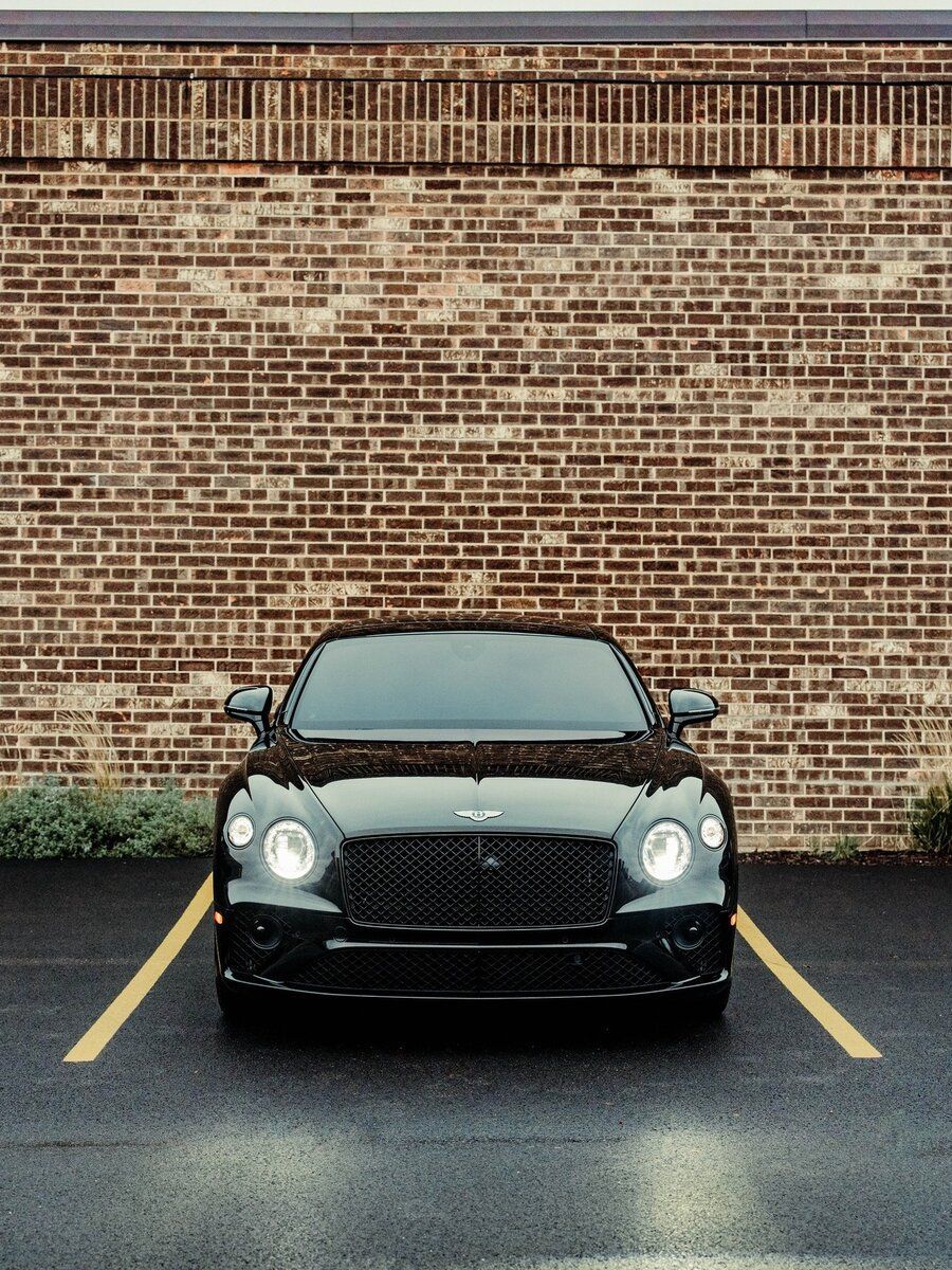 A black car is parked in a parking lot in front of a brick wall.