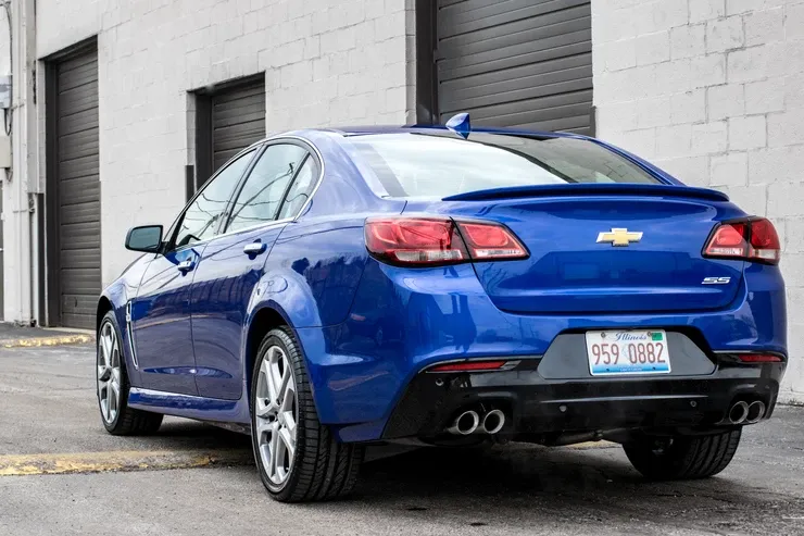 A blue chevrolet sedan is parked in front of a garage door.