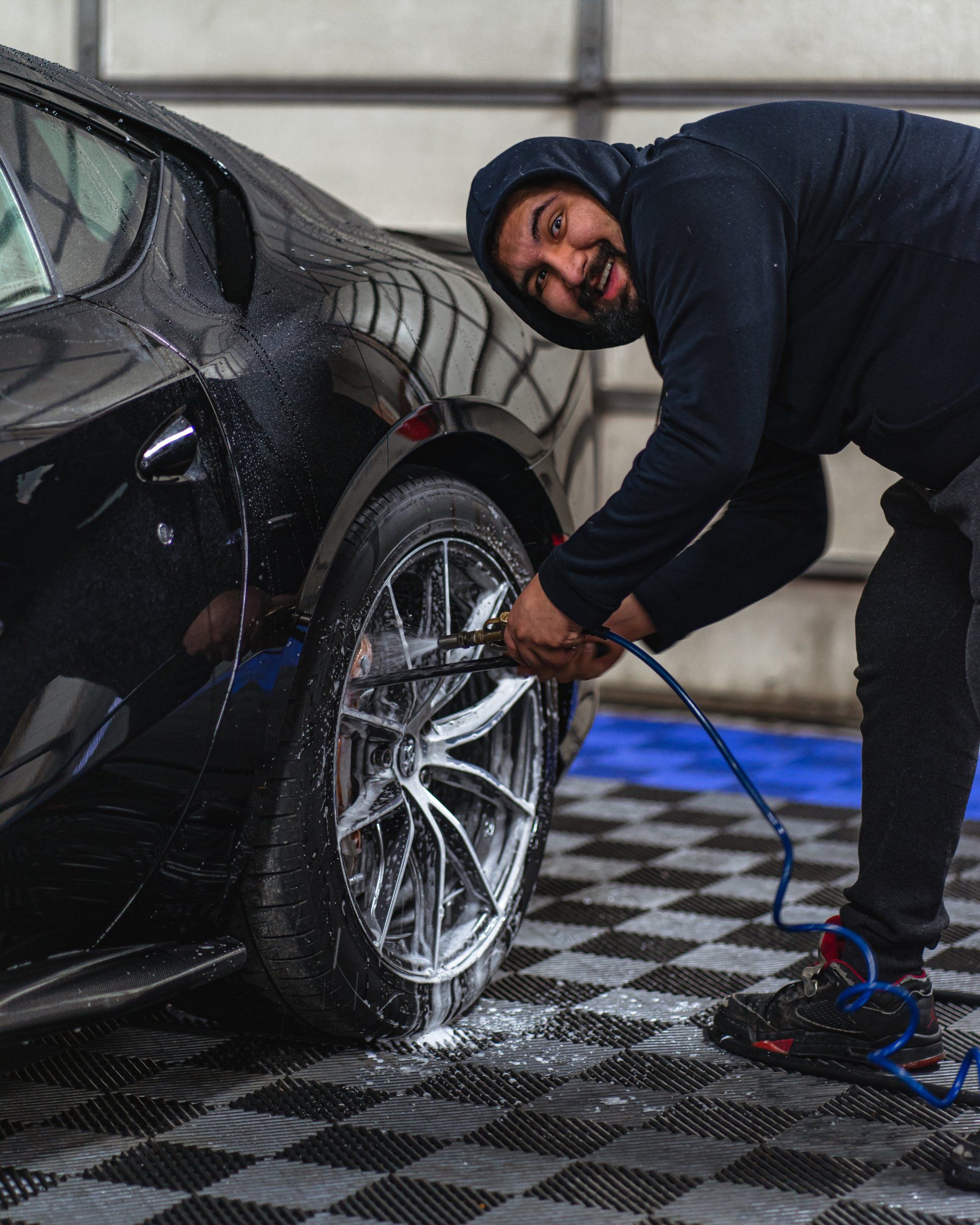 A man is washing a car with a hose in a garage.