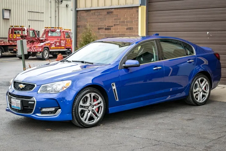 A blue car is parked in front of a garage next to a tow truck.